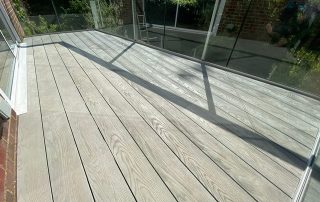 Millboard composite decking in a grey colour called Smoked Oak installed to create a balcony with glass balustrades
