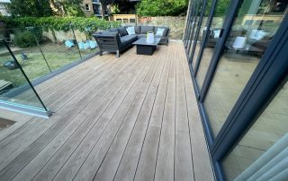 Decking using Millboard decking in Golden Oak with glass balustrades installed to the back garden of a house that has bifold doors