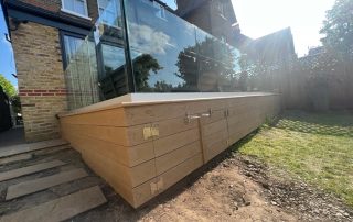 Decking using Millboard decking in Golden Oak with glass balustrades installed to the back garden of a house that has bifold doors