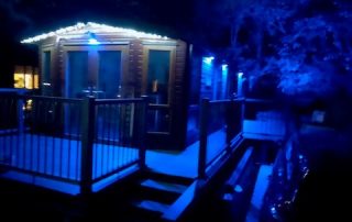 Static home with composite decking surrounding it at night with blue lights