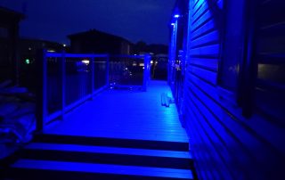 Static home with composite decking surrounding it at night with blue lights