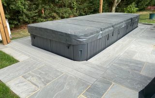 Millboard composite decking installed surrounding a swim spa in a grey colour called smoked oak which is then surrounded by grey patio tiles.