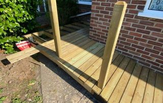 Work in progress installing a ramp and decking with a railing created from timber surrounding a corner of a residential property