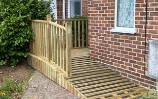 Ramp with grip strips and decking with a railing created from timber surrounding a corner of a residential property