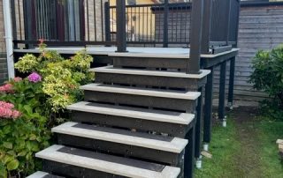 Work in progress building steps leading down to the back garden from the back door of a property created using Millboard's smoked oak decking with a black railing