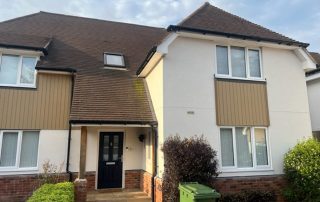 Envirobuild composite cladding installed on the exterior of the first floor of a detached house and below a first floor window in a pale brown